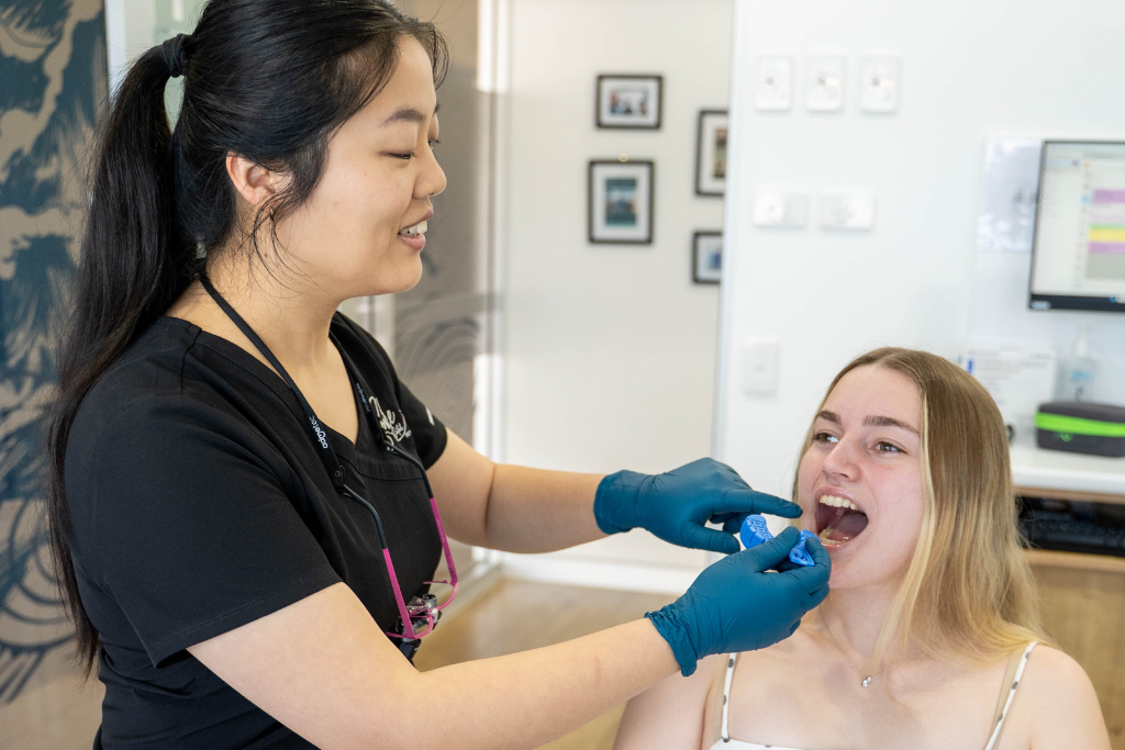 Dental professional in blue gloves examining a patient's open mouth in a dental clinic.
